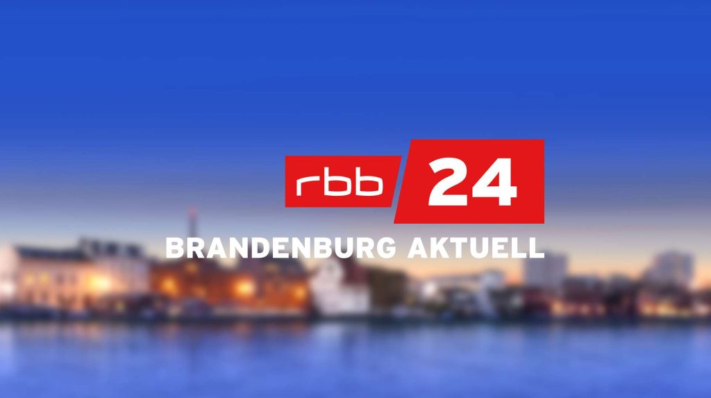 rbb24 Brandenburg aktuell Logo, vor verschwommener Uferlandschaft einer Stadt am Abend.